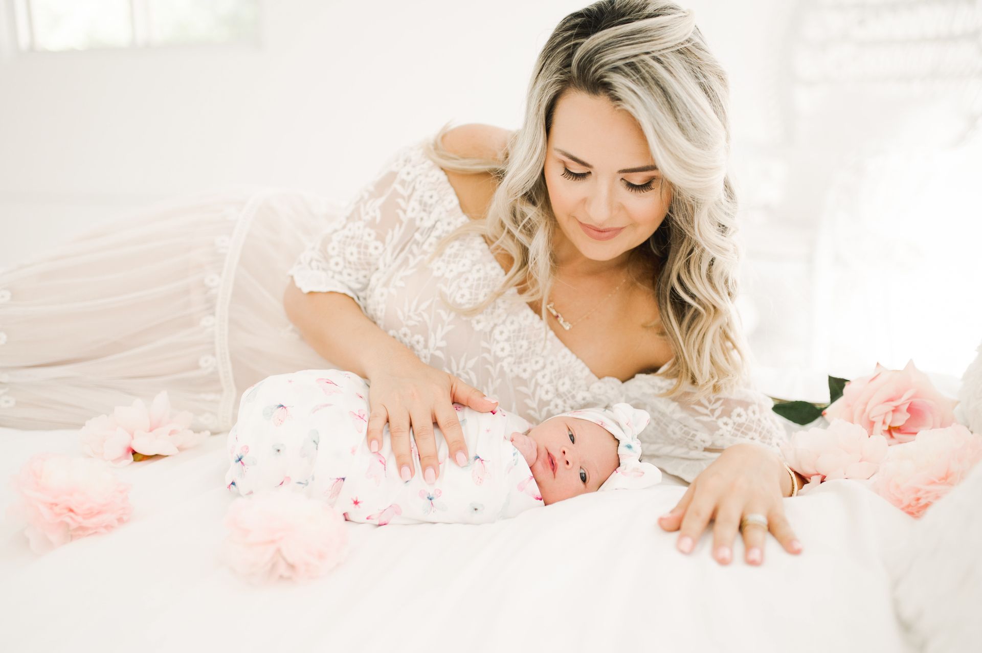 Adult holding a baby in a butterfly-print swaddle beside peonies