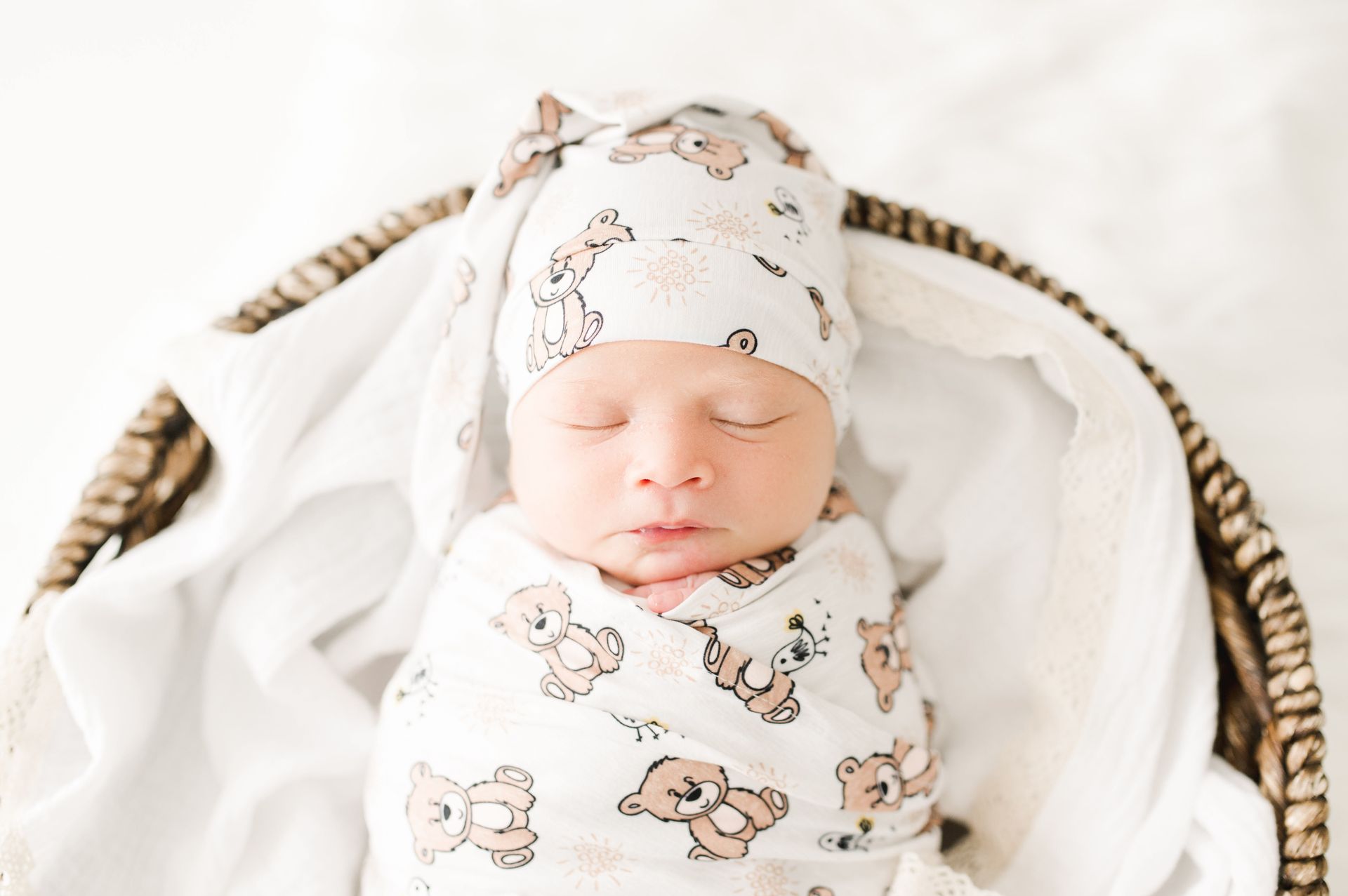 Baby in a teddy-bear-print swaddle and knotted hat in a basket